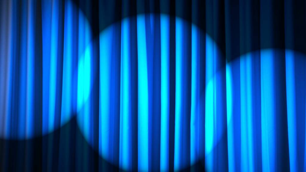 Sinisiin teatteriverhoihin heijastuu kolme valospottia.
